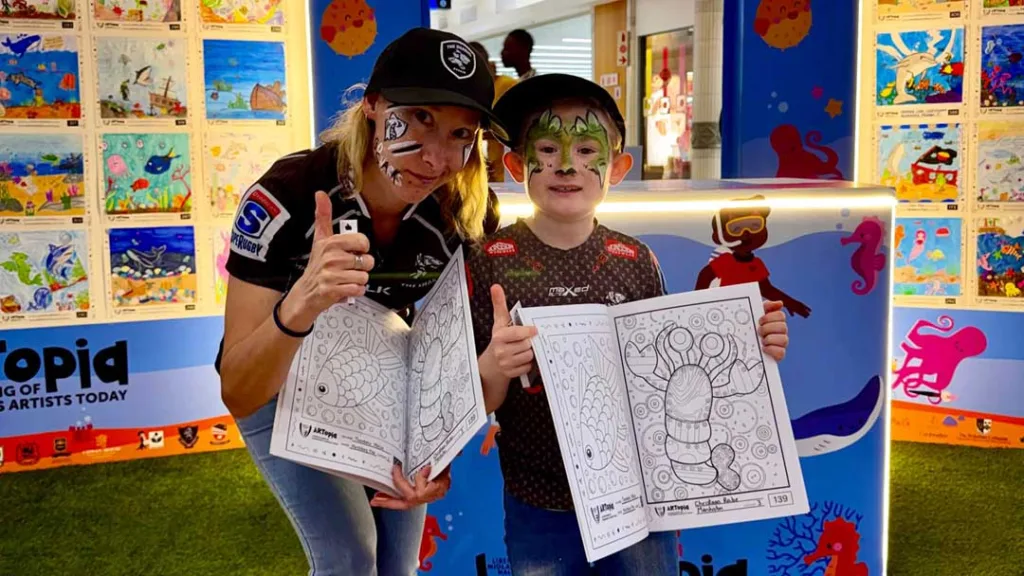 Two face-painted participants hold ARTopia ocean-themed colouring books at Liberty Midlands Mall.